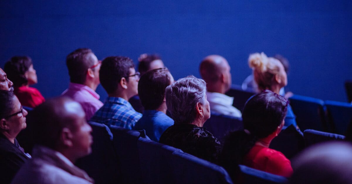 dark conference room with theater seating and people sitting facing the stage