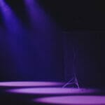 purple lights shine down on a dark stage