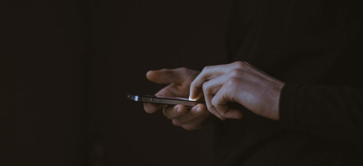 two hands holding an iPhone with a dark background