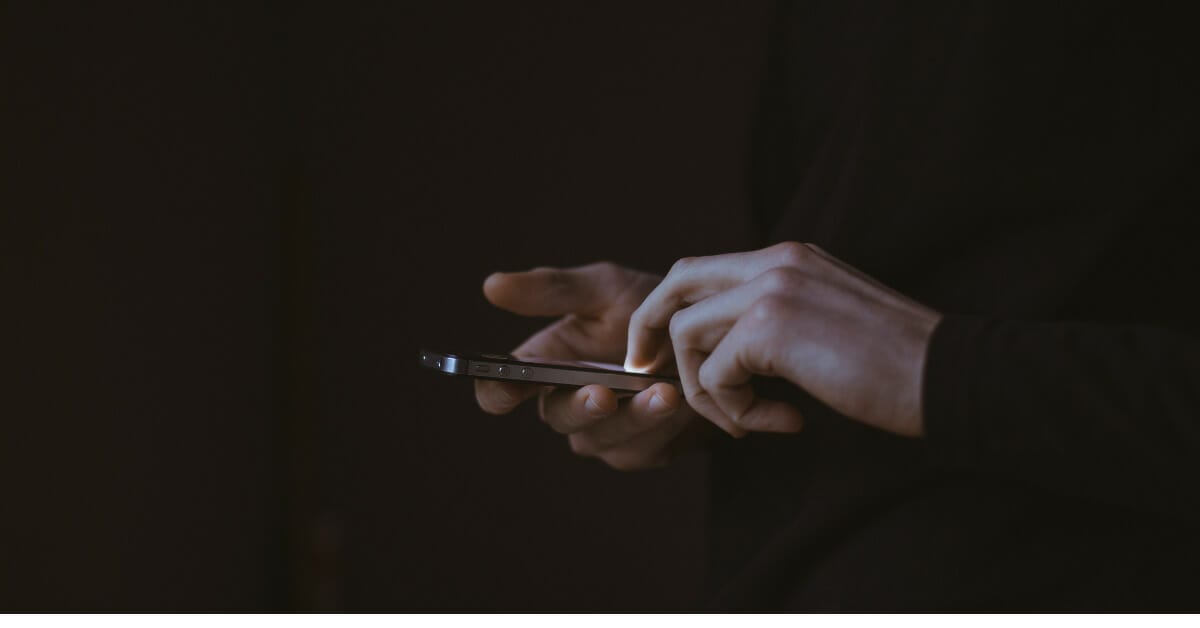 two hands holding an iPhone with a dark background