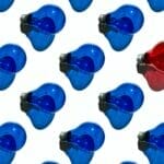 A pattern of lightbulbs against a white background - all the lightbulbs are blue except one that is red