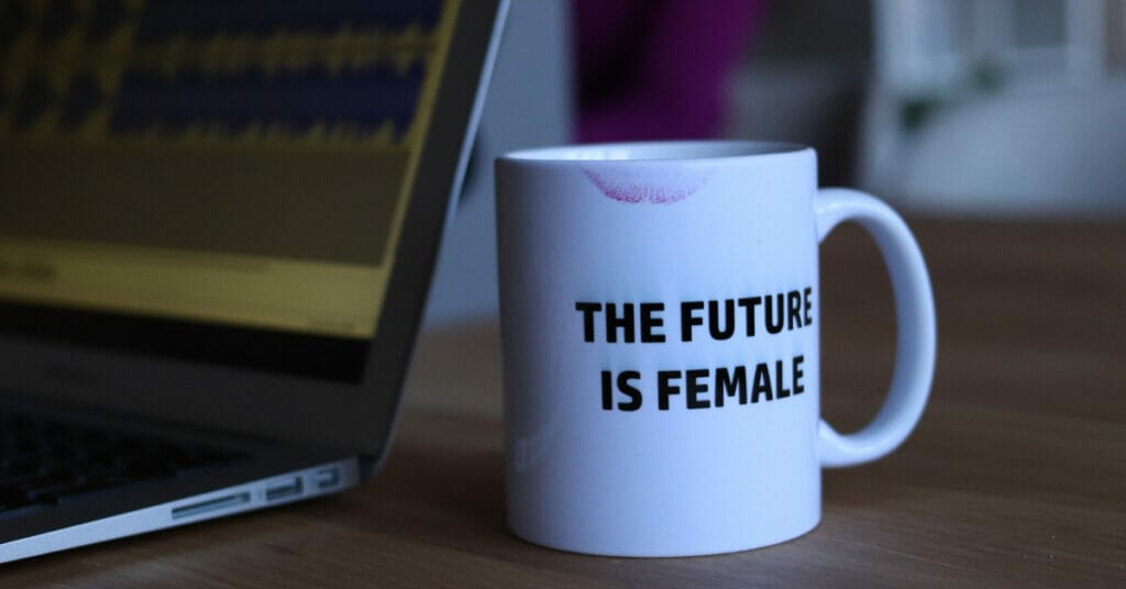 A desk with a laptop and a white mug with a lipstick stain that says The Future is Female