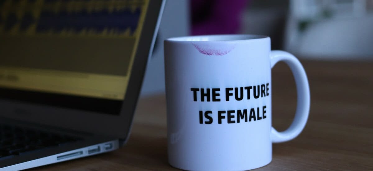 A desk with a laptop and a white mug with a lipstick stain that says The Future is Female