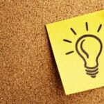 A light bulb drawn onto a post-it note that is pinned onto a corkboard.