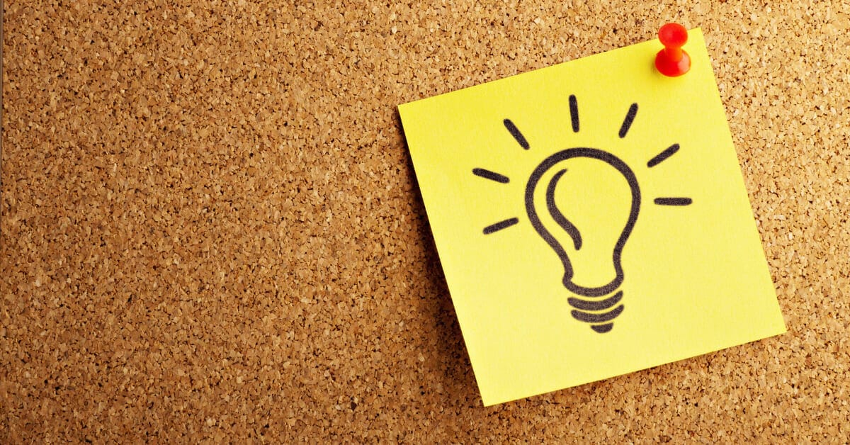 A light bulb drawn onto a post-it note that is pinned onto a corkboard.
