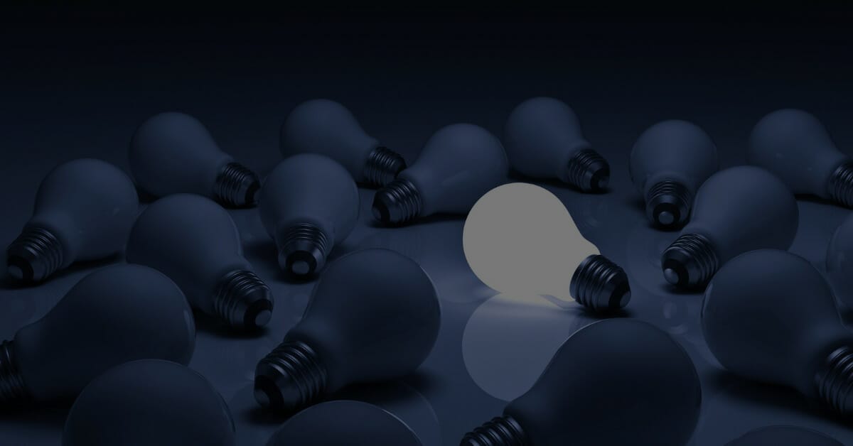 One glowing light bulb standing out from unlit incandescent bulbs.