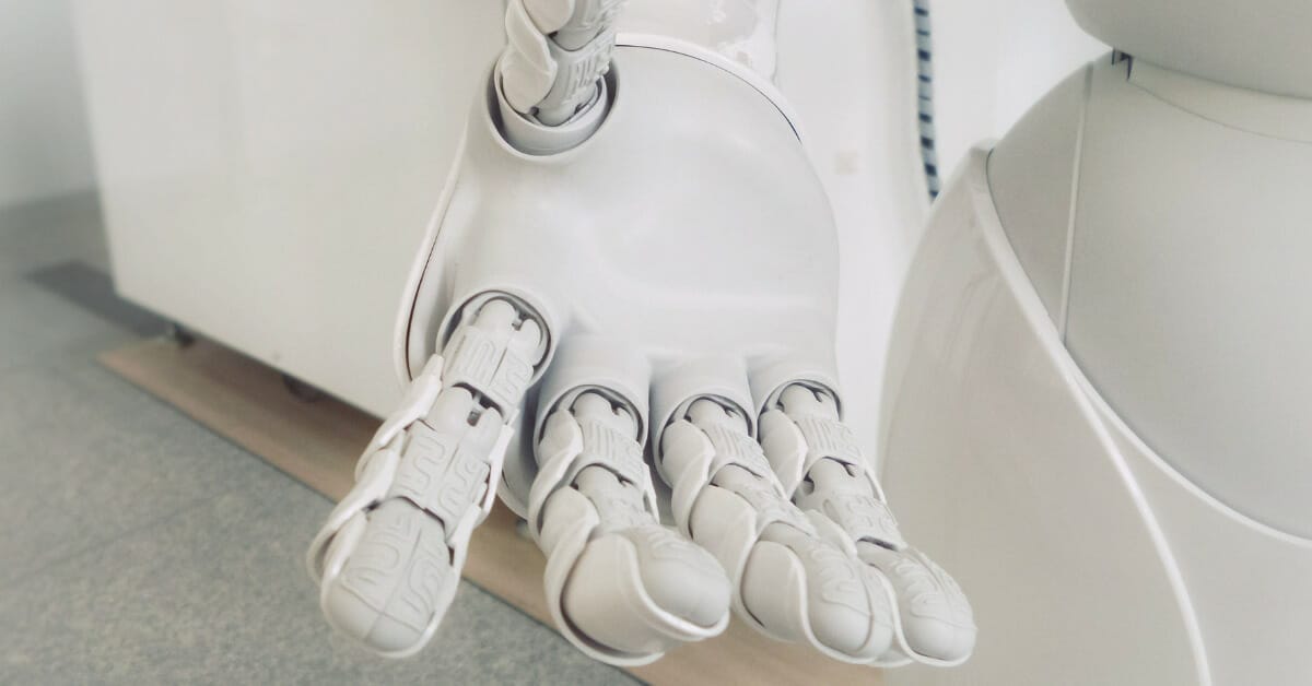 An image of a white robotic hand reaching out to the viewer in front of a white/gray background