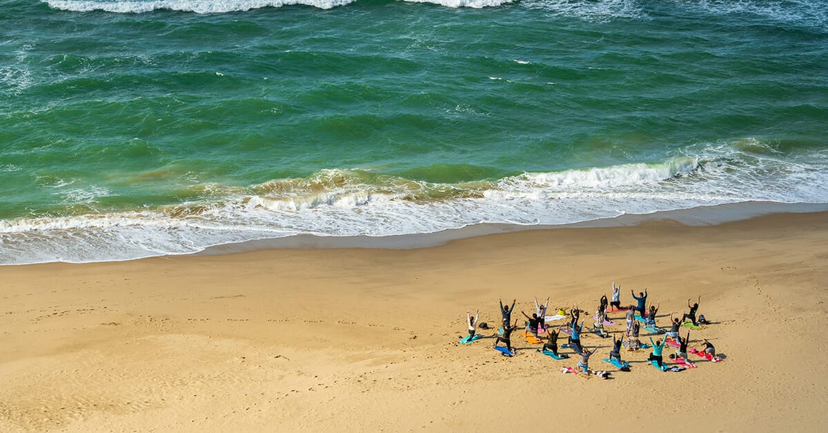 A group of people doing well-being yoga on a beach