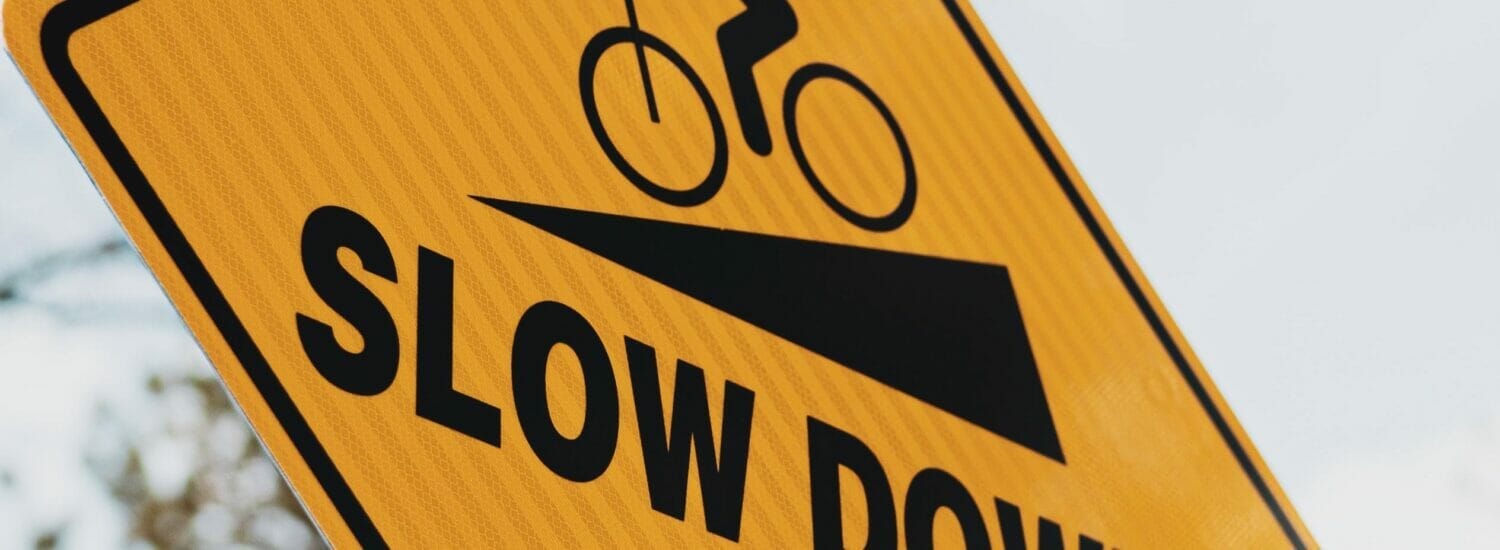 An image of a yellow sign that says SLOW DOWN and shows a person riding a bike down an incline