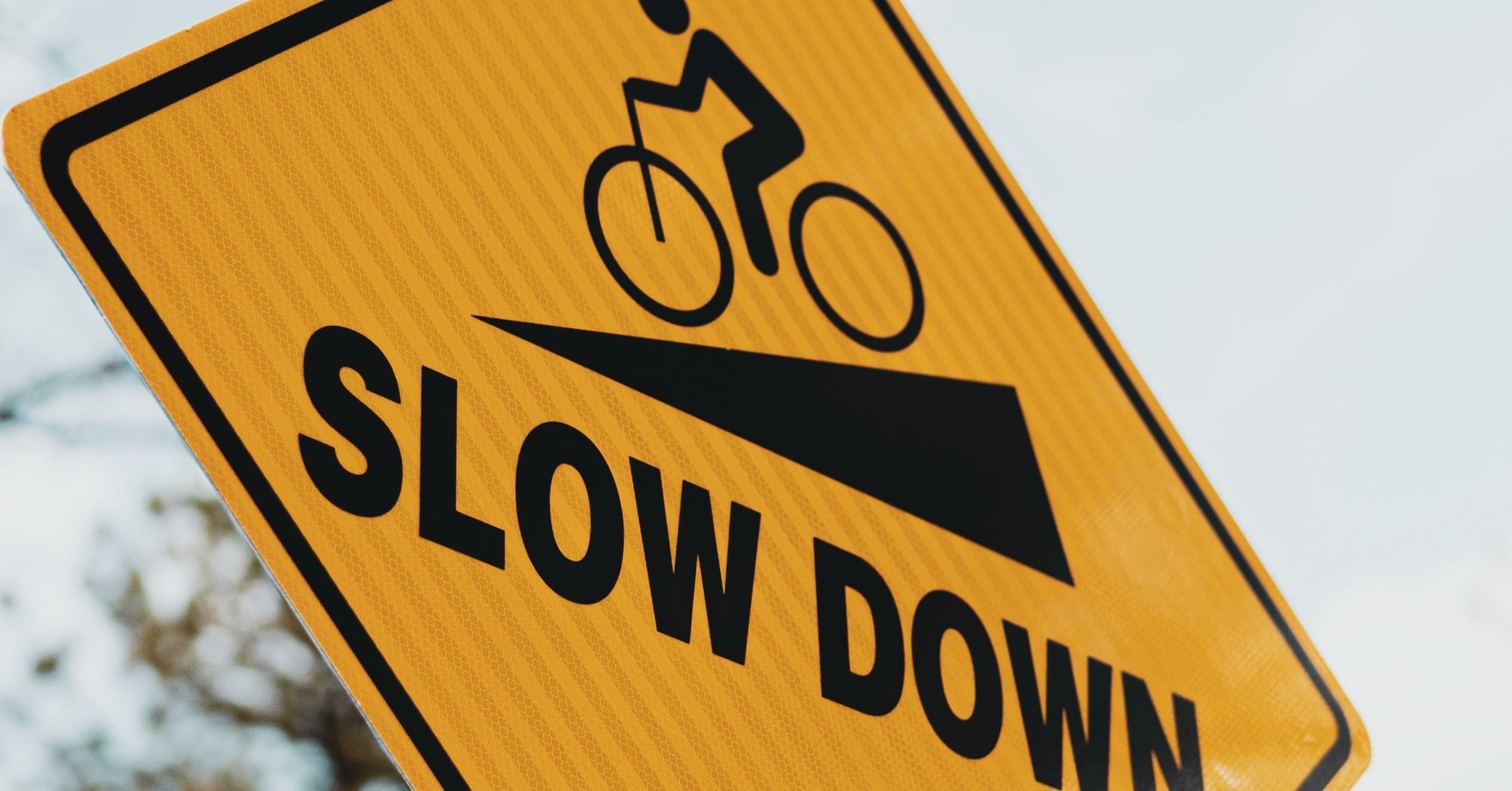 An image of a yellow sign that says SLOW DOWN and shows a person riding a bike down an incline