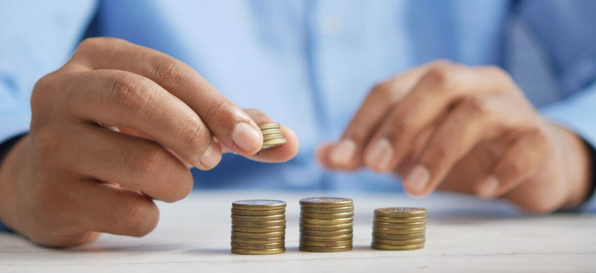 Two hands are making three stacks of golden colored coins