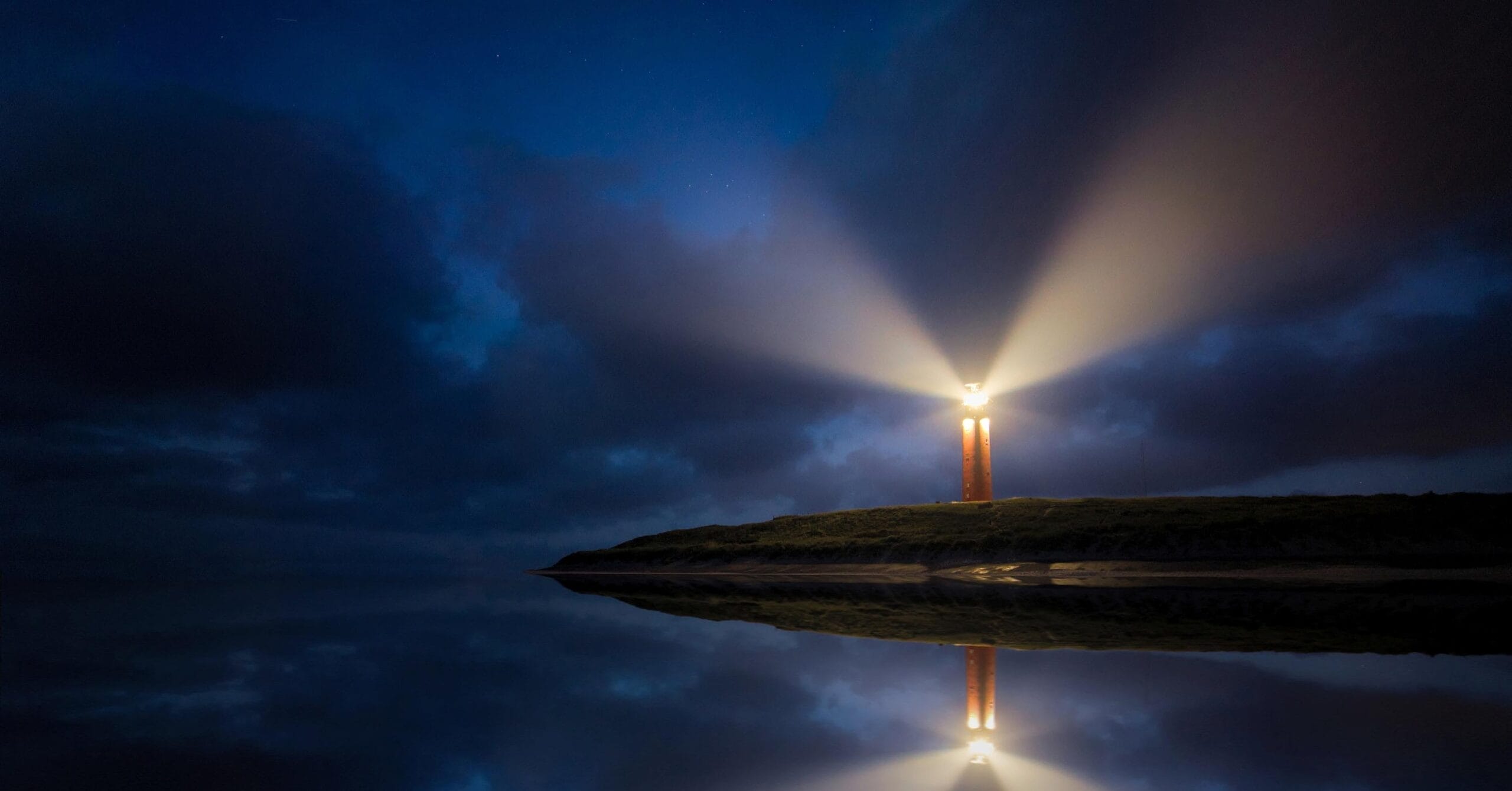 A lighthouse on a jetty sticking out into a body of water, showing light beams, implying hope and resilience