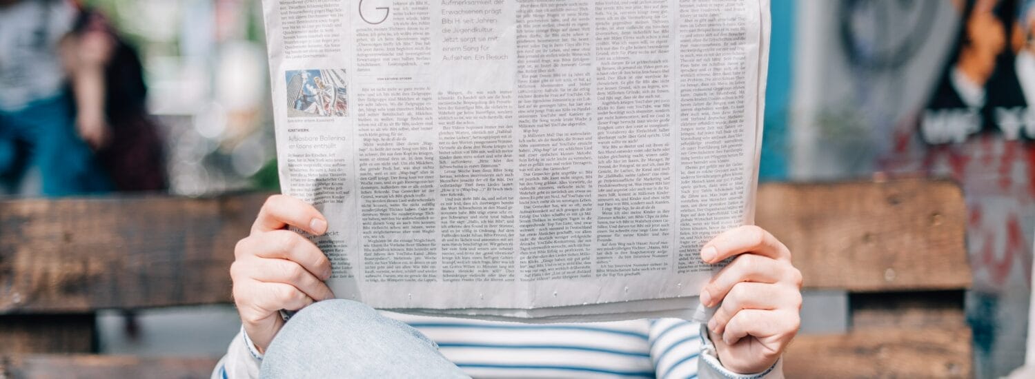 Person sitting on a bench holding a newspaper in front of their face