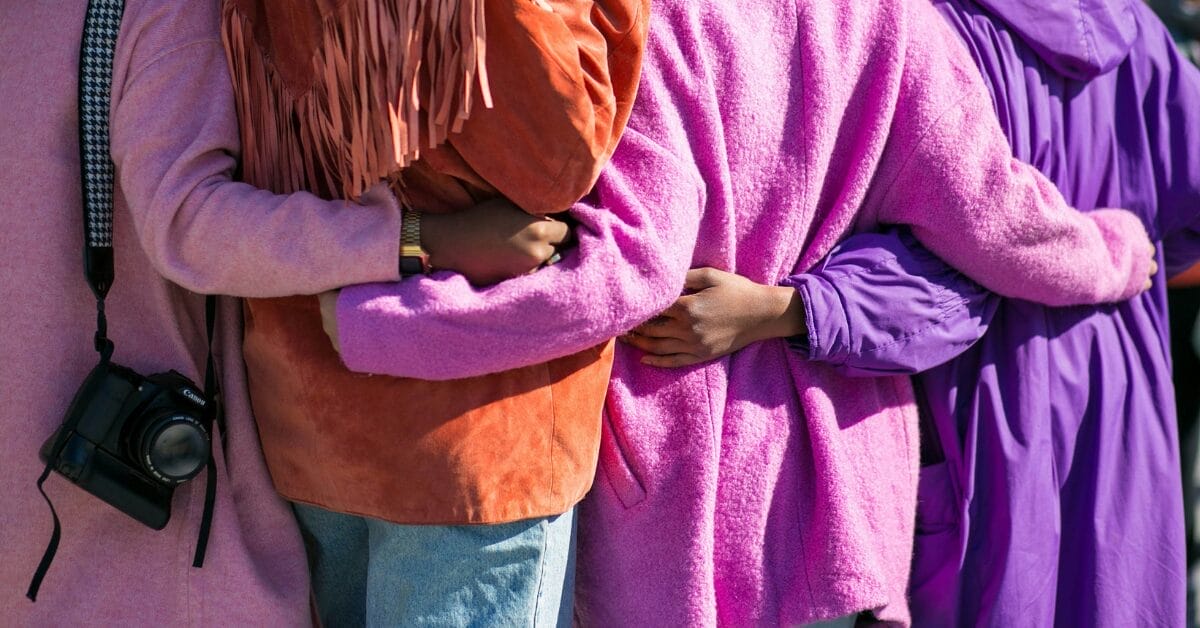 Four people in purple jackets holding hands behind each others backs, showing inclusion