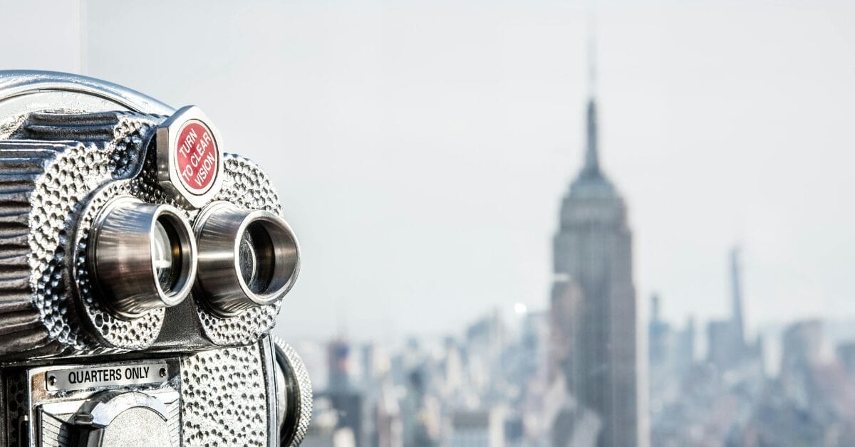 binoculars in the foreground with new york and the empire state building in the background, signifying visibility
